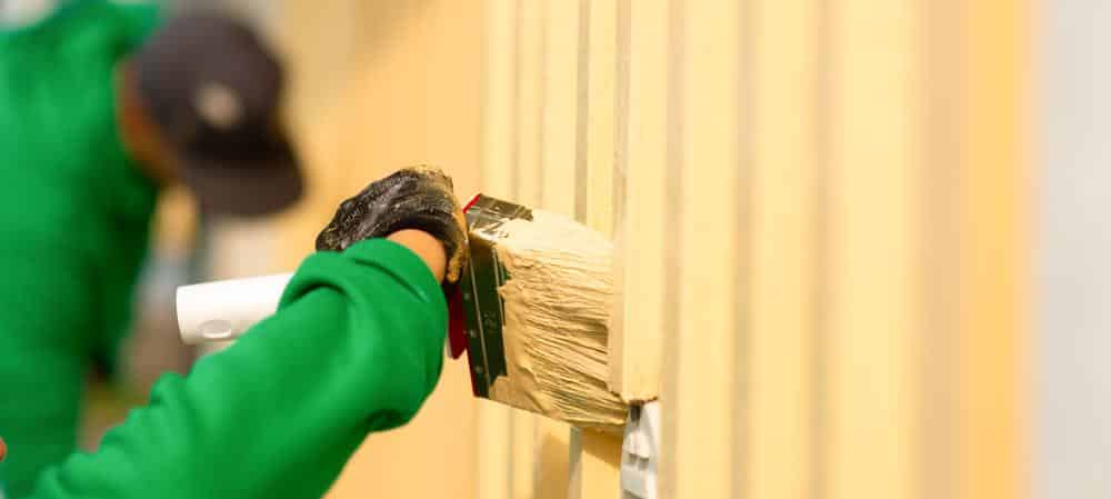 Maalari maalaa keltaisella maalilla talon ulkoseinää